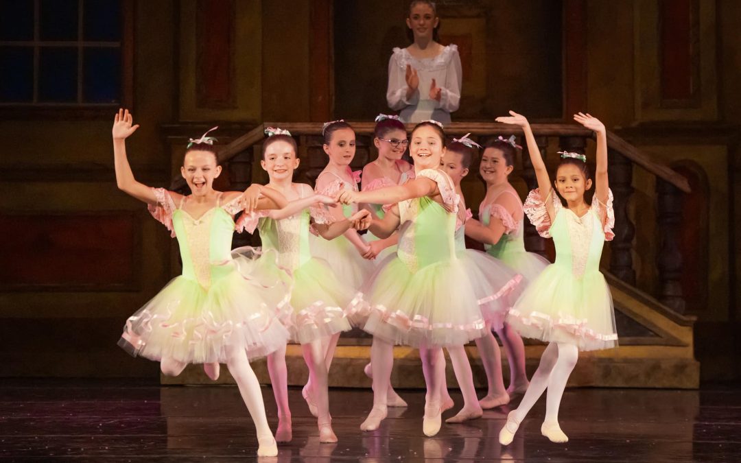 Eight children ballet dancers on stage looking at audience and smiling while performing nutcracker